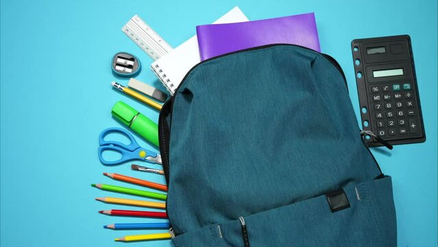 From the school bag appear colorful school supplies on blue background. Back to school concept. Stop motion