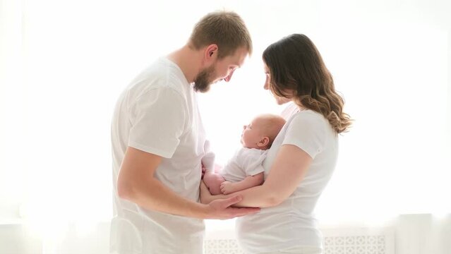 A happy young family mom dad and a small child smiling and kissing on a white isolated window background, a loving family threesome at home