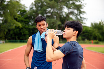 During sports training on a running track, two male athletes underscore the importance of hydration...