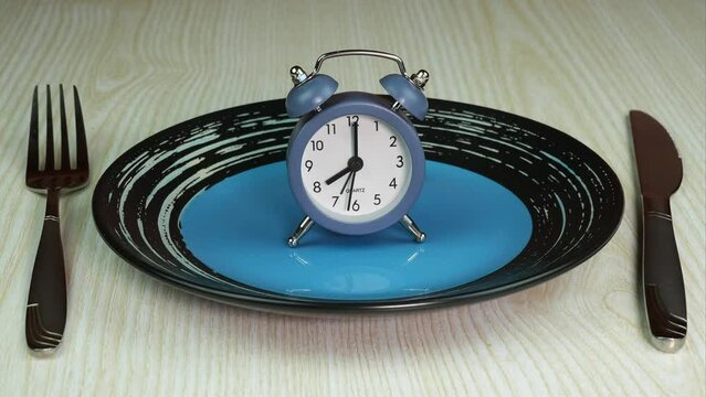 View from above on empty blue and black plate with alarm clock. Knife and fork near. Concept of food, losing weight and eating on time. Stop Motion