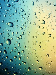 Close-up of clear raindrops on a blue to yellow gradient glass surface.