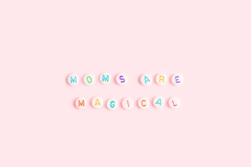 Moms are magical. Quote made of white round beads with multicolored letters on a pink background.