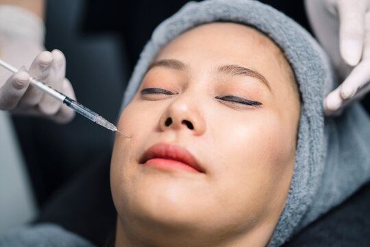 clinic person injecting asian woman rejuvenate face skin. beautiful patient got facial treatment injection using syringe by staff. surgeon using needle injecting medicine to patient for young face