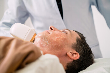 surgeon using peeling machine caucasian man skin. male patient got ultrasonic treatment on face for young skin lifting. surgeon using ultrasound tool for cleansing patient recovery smooth care face