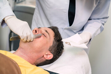 Fototapeta premium clinic surgeon cleaning caucasian man face from lotion. male patient after cosmetology therapy got collagen cream removal. surgeon using metal tool to clean up lotion cream from patient handsome face