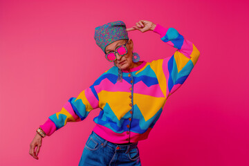 elderly woman dressed in colorful funky dress on pink background