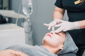 surgery person putting cream woman face for treatment. female asian patient relax after facial treatment and staff applying mask. surgeon using mask cream rubbing on calm sleep patient beautiful face