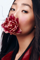 Beautiful Asian woman with long black hair posing with flower in front of her mouth