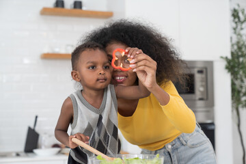 African American young mother cooking with little son in kitchen room at home