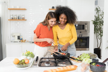 Two young woman cooking salad together in kitchen room at home