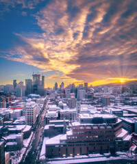 Purple sunset and colourful cloudscape above Saint-Catherine Street, downtown Montreal skyline covered in snow, and rays above Mount Royal, Quebec, Canada. Vertical winter photo taken in February 2023