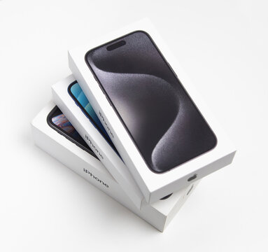 Apple iPhones in boxes, stacked on white desk. iPhone 15 Pro on top.