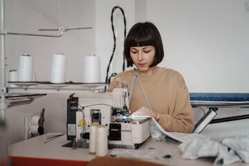 A 35-year-old woman attentively sews clothing in her cozy workshop.