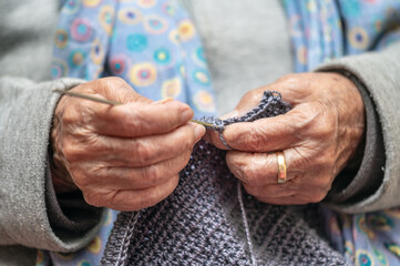 Close up of a mature woman knitting at home, enjoying leisure time, holding needles, elderly generation hobby activity. High quality photo