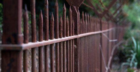 Rusty fencing with vertical bars and a V-shape with barbed wire at the top to make climbing over it impossible. Narrow depth of field, blurred on the right for copy space