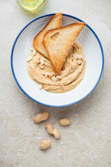 Blue and white plate with peanut butter and toasts, vertical shot on a beige stone background, above view