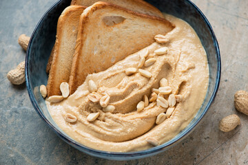 Blue bowl with peanut butter and toasted bread, horizontal shot on a beige and grey granite...