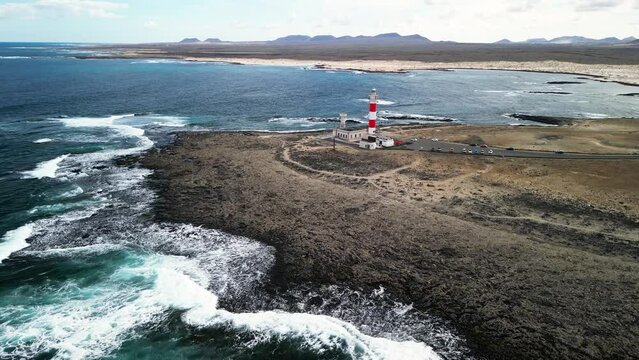The ocean waves hits the rocky coast next to the El Cotillo Lighthouse, Fuerteventura, Canary Islands, Spain. High-quality drone footage. 
