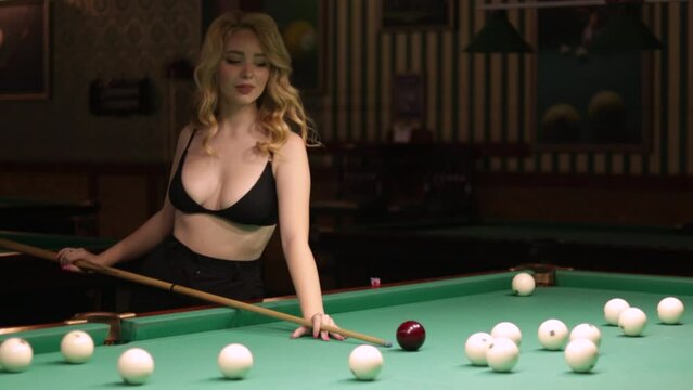 Blond woman playing enjoying billiard, hold cue hit white billiard balls on table with green surface in billiard club. Pool game snooker pyramid player

