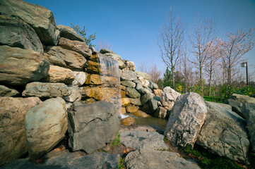 Authentic landscape overlooking a spring garden and artificial waterfall with flowing water and stone structures. 