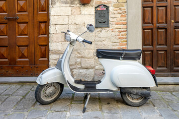 Old white piaggio vespa scooter parked in the street of an old Italian town 