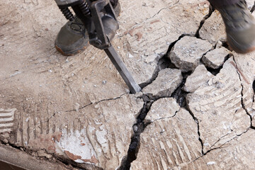 Construction worker chisels the concrete slab with a hammer drill