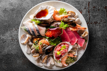 Assorted fresh sashimi, including tuna and shrimp, elegantly presented on a plate with garnishes,...