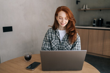 Portrait of smiling female freelancer looking at laptop screen, reading good news in message, watching video, chatting in social network or shopping online at home, enjoying leisure time with computer