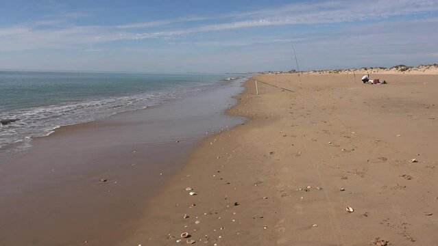 Fisherman on a beach with dunes, empty of people, with several fishing rods  