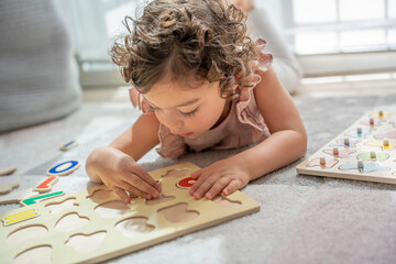 Close-up image of a little girl lying on a play mat playing with a wooden alphabet letter puzzle....