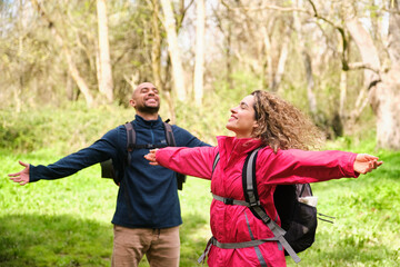 A woman and a man are standing in a forest, breathing and enjoying the moment. Wellbeing, wellness,...