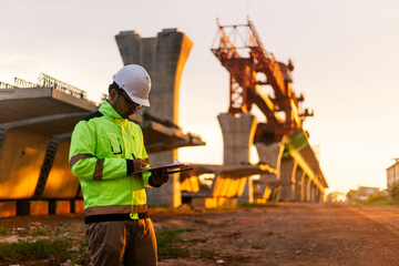 A construction worker is standing on a bridge, talking on his cell phone. The scene is set in a construction site, with a large crane in the background. The worker is wearing a yellow jacket
