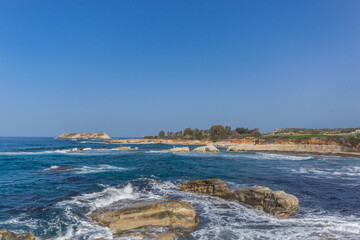 Waves Crashing on Rocky Beach. The white foamy spray contrasts with the dark tones of the rocks, illustrating the harsh beauty of the coastal landscape