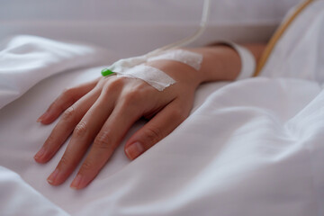 Close-up of an adult hand with IV line, soft focus on white linen, conveying a sense of medical...