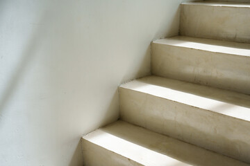 Sunlit stair corner, white walls, play of light and shadow, embodies quietude, simplicity in...