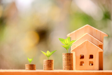 Home model and stack gold coin with plant growing interest put on the wood in the public park, Business investment loan for real estate or save money for buy new house in the future concept.