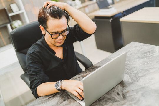 Upset Asian business man stressed and headache. tired office man hand on head confused from busy too much thought to work late and got office syndrome. exhausted employee touch head using laptop work