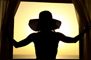Silhouette of a girl on a loggia balcony background. A happy woman with a hat in her hands while on vacation traveling.