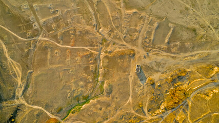 Traces of dirt roads and ruined houses mark the site of a former village, now submerged beneath the reservoir formed by a breached dam, with only the surviving church of St. Ivan Rilski, Bulgaria