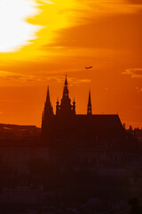 Commercial airline jet flying behind Prague Castle at sunset, dramatic orange sky in Prague, 