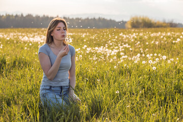 Portrait of a beautiful young woman blowing a dandelion in a flower meadow. Femininity and freedom concepts.