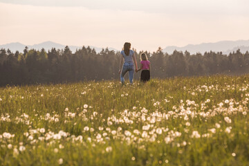 Mother and her little daughter walking in the meadow into the sunset light.