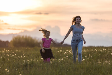 Mother and her little daughter running holding hands in the beautiful nature at the setting sun.