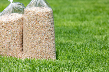 Bags of lawn fertilizer and herbicide in yard with healthy grass. Lawn care, weed control and...