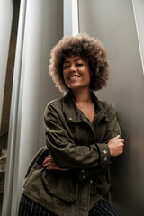 Mixed race curly woman leaning on metallic wall.