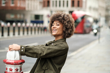 Smiling curly woman holding on a bollard outdoors.
