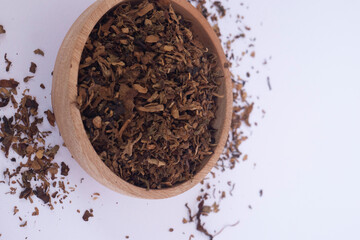 Tobacco granules in a wooden bowl on a white background.