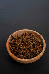 tobacco leaf granules on a wooden bowl with black isolated object. 45 degrees view.
