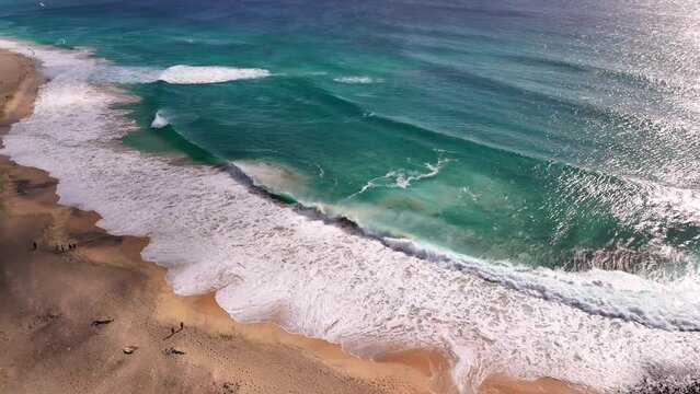 Overview of the stand line in Ponta Preta, Sal, Cape Verde, as large waves break and churn up the sea. Kites and a piece of Santa Maria can be seen
