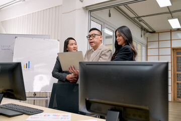 Asian business team working to discuss plan with single laptop in office meeting room.